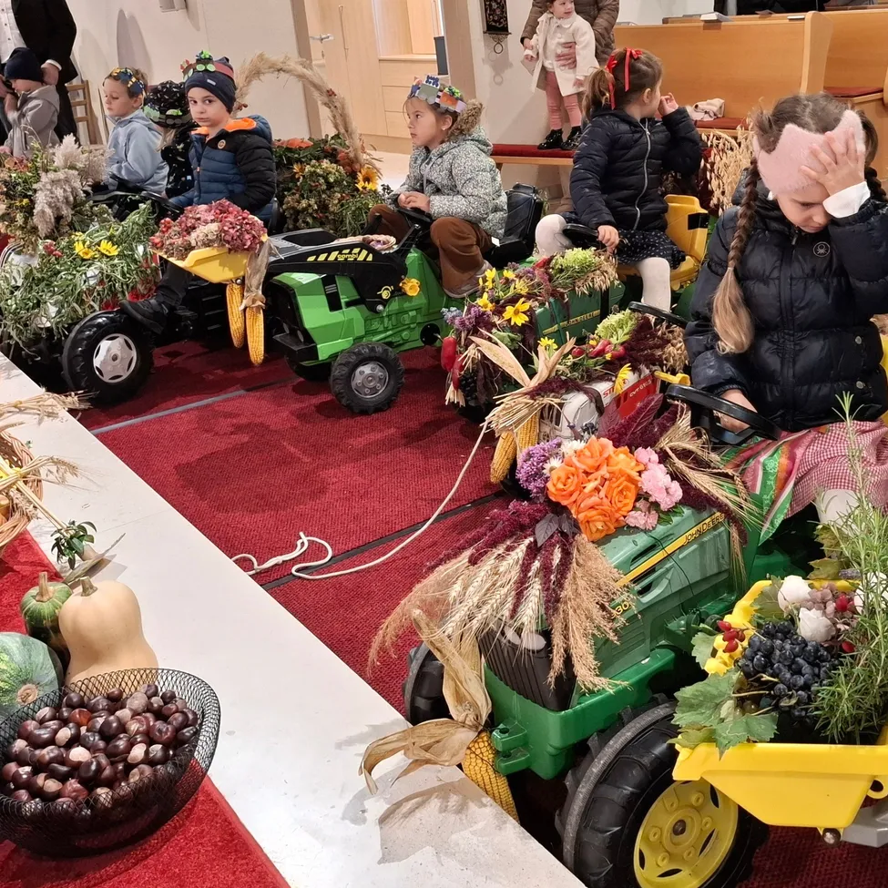 Mehrere Kinder in Winterkleidung fahren auf mit Blumen und Früchten geschmückten Spielzeugtraktoren in einer festlichen Umgebung.