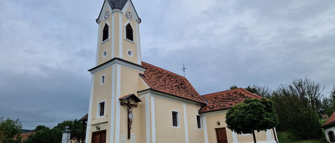 Eine traditionelle Kirche mit einem Turm und einem Kreuz darauf. Es hat ein Ziegeldach und einen Holzzaun davor.