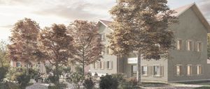 Ein Outdoor-Café-Bereich mit Menschen, die an Tischen sitzen. Die Umgebung zeigt ein modernes Gebäude mit Backsteinwänden, einem roten Dach und einem Schild mit der Aufschrift 'Gasthof Frei'. Bäume mit Herbstlaub und Sonnenschirme ergänzen die Szene.