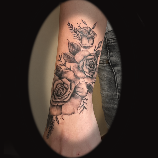 Am Unterarm einer Person ist ein Tattoo von drei Rosen in Schwarz-Weiß mit Blättern und Stielen zu sehen. Das Tattoo ist detailliert und kunstvoll.