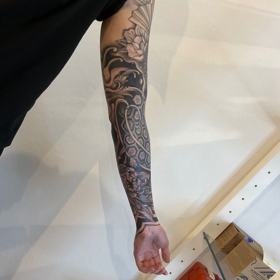 Eine Person mit einem Ärmeltattoo am rechten Arm, das ein geometrisches Muster mit Blumen und Sechsecken zeigt.