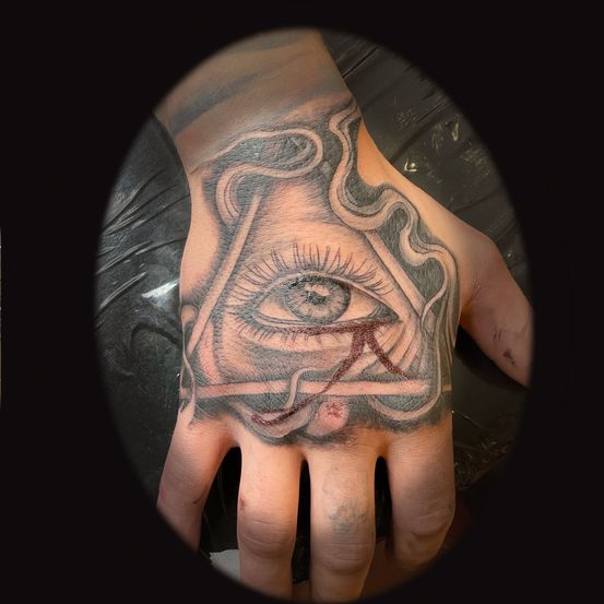 Eine Hand mit einem detaillierten Tattoo eines Auges in einem Dreieck auf dem Handrücken.