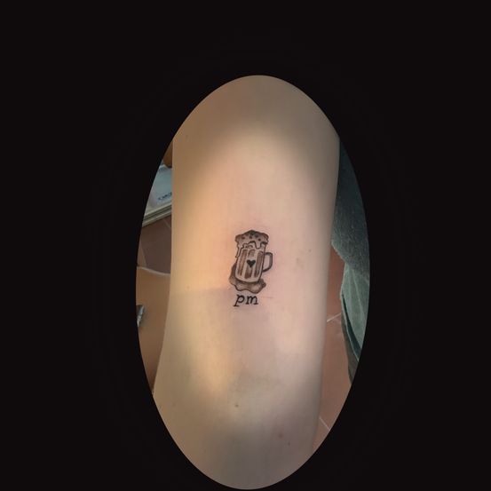 Tattoo eines Bierglases mit einem Herz auf dem Arm einer Person, darunter die Initialen 'pm'.