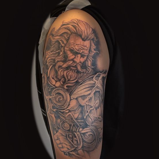 Eine Tätowierung eines alten Kriegers mit Bart und ernstem Gesichtsausdruck, der einen Hammer und einen Schild hält. Der Hintergrund ist dunkel.