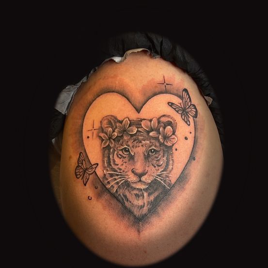 Ein Herztattoo mit dem Gesicht eines Tigers, umgeben von Blumen und Schmetterlingen. Es hat ein Kreuz auf der linken und rechten Seite.