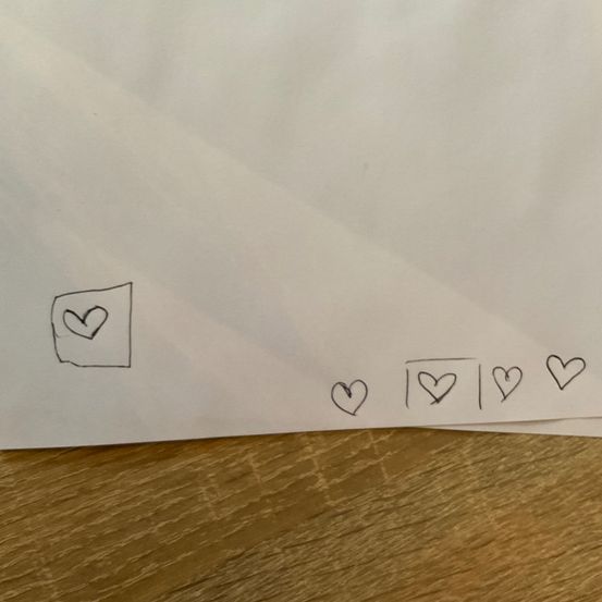Ein weißes Blatt Papier mit einem Herzen in der Ecke und vier weiteren Herzen in einer Reihe darunter liegt auf einer Holzoberfläche.