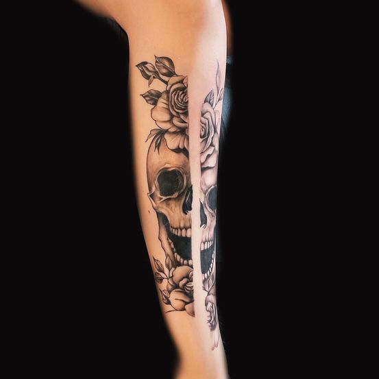 Ein schwarz-weißes Totenkopf-Tattoo mit Rosen auf dem Arm. Es ist zur Hälfte schwarz und zur Hälfte weiß.
