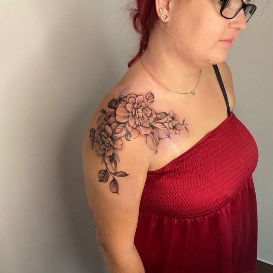 Eine Frau mit roten Haaren trägt ein rotes Kleid. Sie hat ein Blumentattoo auf ihrer Schulter.