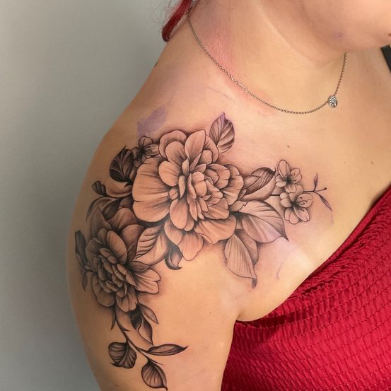Die Schulter einer Frau zeigt ein detailliertes Tattoo von Blumen mit verschiedenen Brauntönen. Das Tattoo erstreckt sich von ihrer Schulter bis zu ihrer Brust.