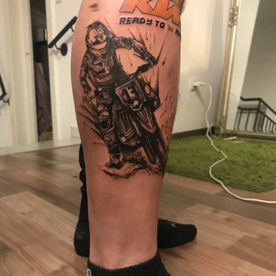 Ein Bein-Tattoo eines Motocross-Fahrers mit der Nummer 15 auf der Brust. Das Wort 'BEREIT' steht über ihm.