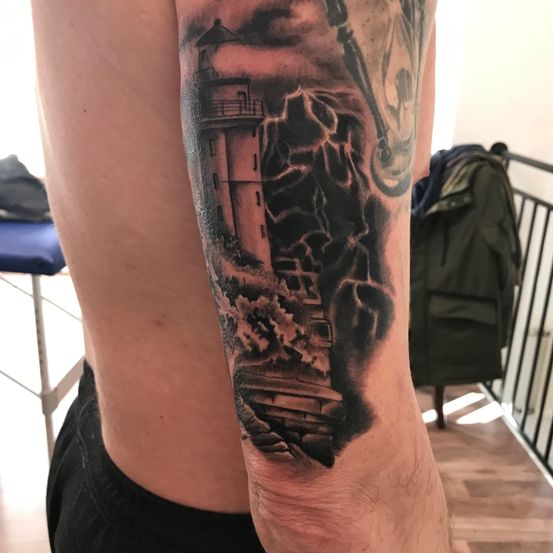 Der Unterarm eines Mannes zeigt ein detailliertes Tattoo eines Leuchtturms, von Blitzen umgeben. Der Hintergrund besteht aus Wolken und Wellen.