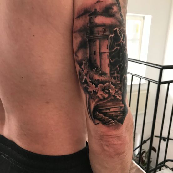 Der Arm einer Person zeigt ein detailliertes Tattoo eines Leuchtturms bei stürmischem Wetter, umgeben von Wellen und Blitzen.