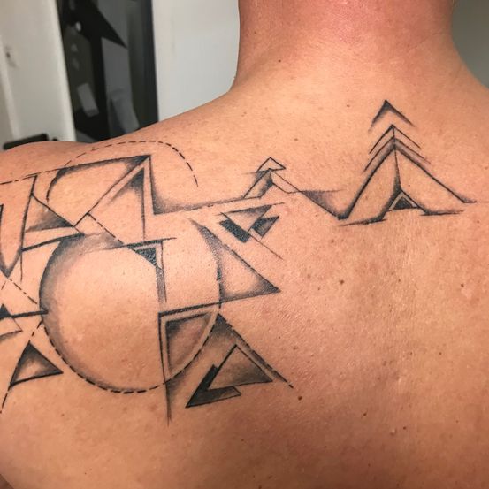 Ein Tattoo auf dem Rücken zeigt ein geometrisches Design mit Dreiecken und einem Kreis, das an eine Bergkette erinnert.
