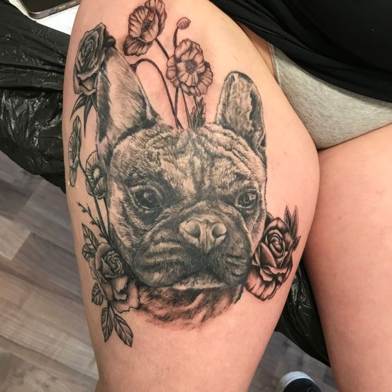 Ein Nahaufnahme eines schwarz-weißen Tattoos eines Französischen Bulldoggens mit floralen Elementen am oberen Oberschenkel.