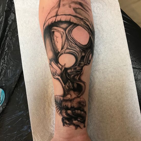 Ein Gasmasken-Tattoo am Unterarm, mit detaillierter Schattierung und Rauch, der aus der Maske aufsteigt. Der Tätowierer verwendete schwarze Tinte.
