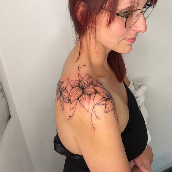 Eine Frau mit roten Haaren und Brille schaut nach unten. Sie hat ein Blumentattoo auf ihrer Schulter.