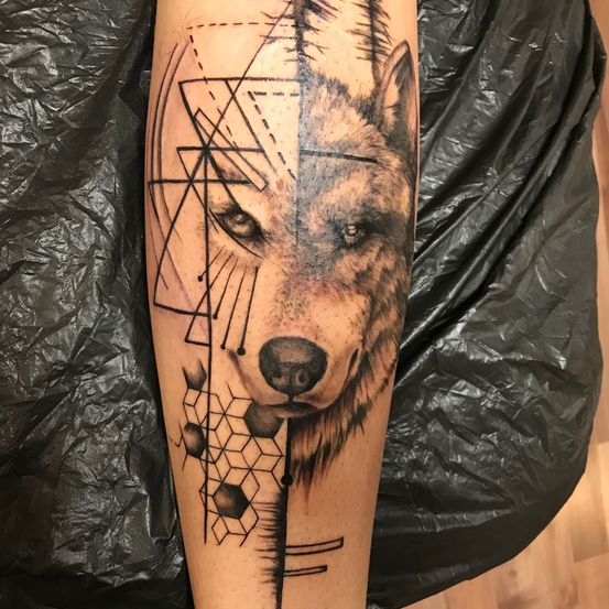 Ein Wolfstattoo mit geometrischen Mustern am Bein, mit detailliertem Gesicht und abstrakten Designs.