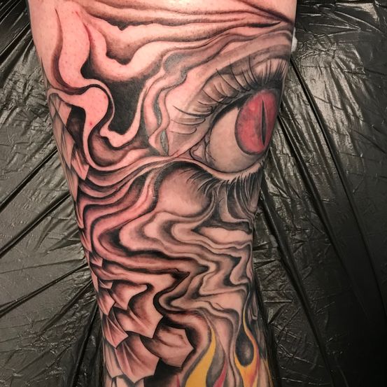 Ein Nahaufnahme einer Person zeigt ein detailliertes Tattoo auf dem Arm, das ein Gesicht mit einem Auge und Rauch oder Flammen im Hintergrund darstellt.