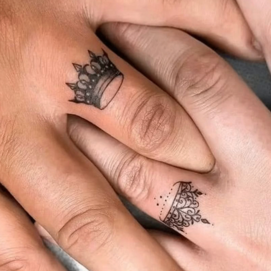 Zwei Hände sind zu sehen, beide mit passenden Kronen-Tattoos auf den Ringfingern. Ein Tattoo ist größer auf der linken Hand und das andere ist kleiner auf der rechten Hand.