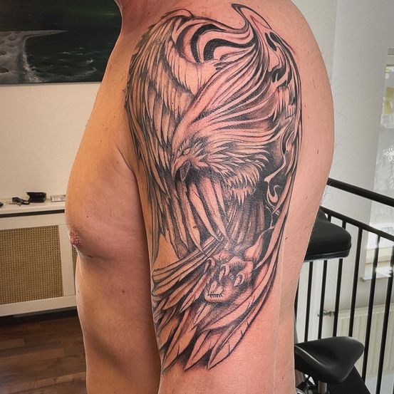 Der Oberarm eines Mannes zeigt ein detailliertes Tattoo eines mythischen Adlers mit weit ausgebreiteten Flügeln, dessen Krallen eine Schlange greifen, vor dem Hintergrund eines Raumes mit Holzböden und einer weißen Wand.