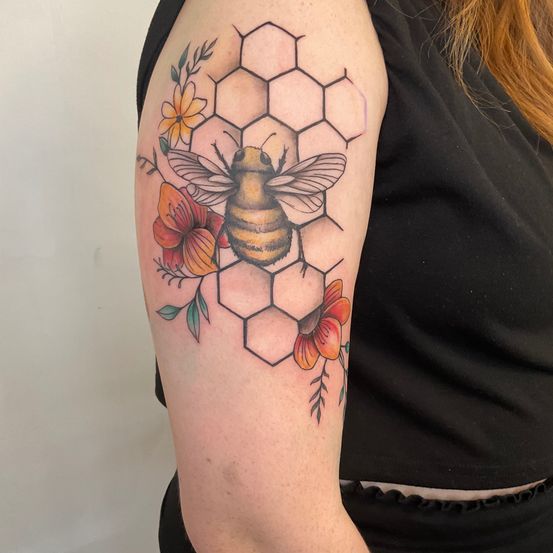Eine Frau zeigt ein Tattoo einer Biene umgeben von Blumen und Hexagonen auf ihrem Oberarm.