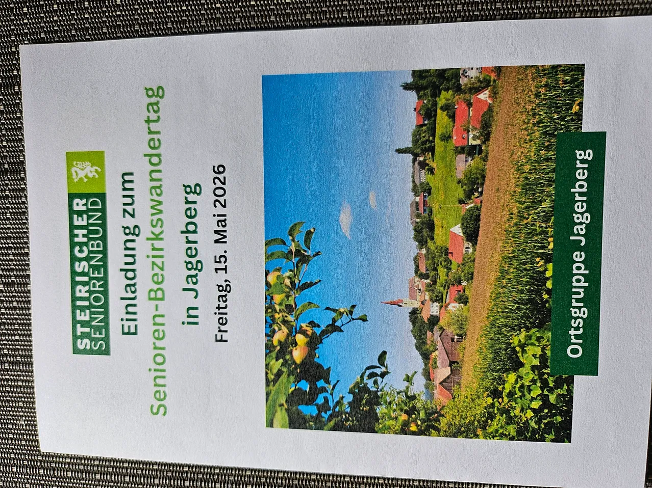 Poster für eine Senioren-Tour am 15. Mai 2026 mit einer ländlichen Landschaft, grünen Feldern, rotgedeckten Häusern und klarem blauem Himmel.