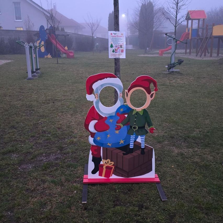 Ein nebliger Morgen mit einer Weihnachtsausschnitt von Santa und einem Elfen, der auf einem geschenkgefüllten Schornstein auf einem Rasen in der Nähe eines Spielplatzes steht.