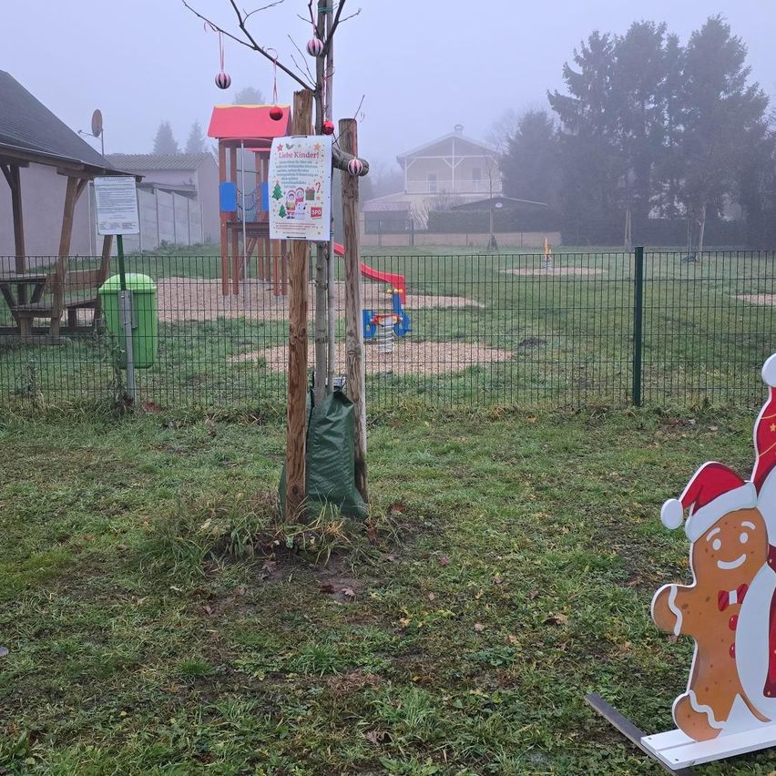 Ein eingezäunter Spielplatz mit Lebkuchenmann- und Weihnachtsmanndekorationen, einem neuen Baum und einem Schild in einem nebligen Morgen.