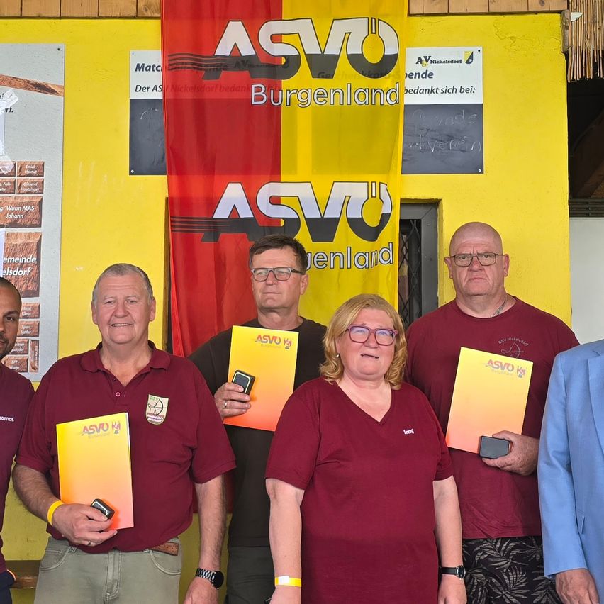 Five adults stand in front of a yellow wall, holding certificates and smiling. A banner with the text ASVO Burgenland is hanging behind them.