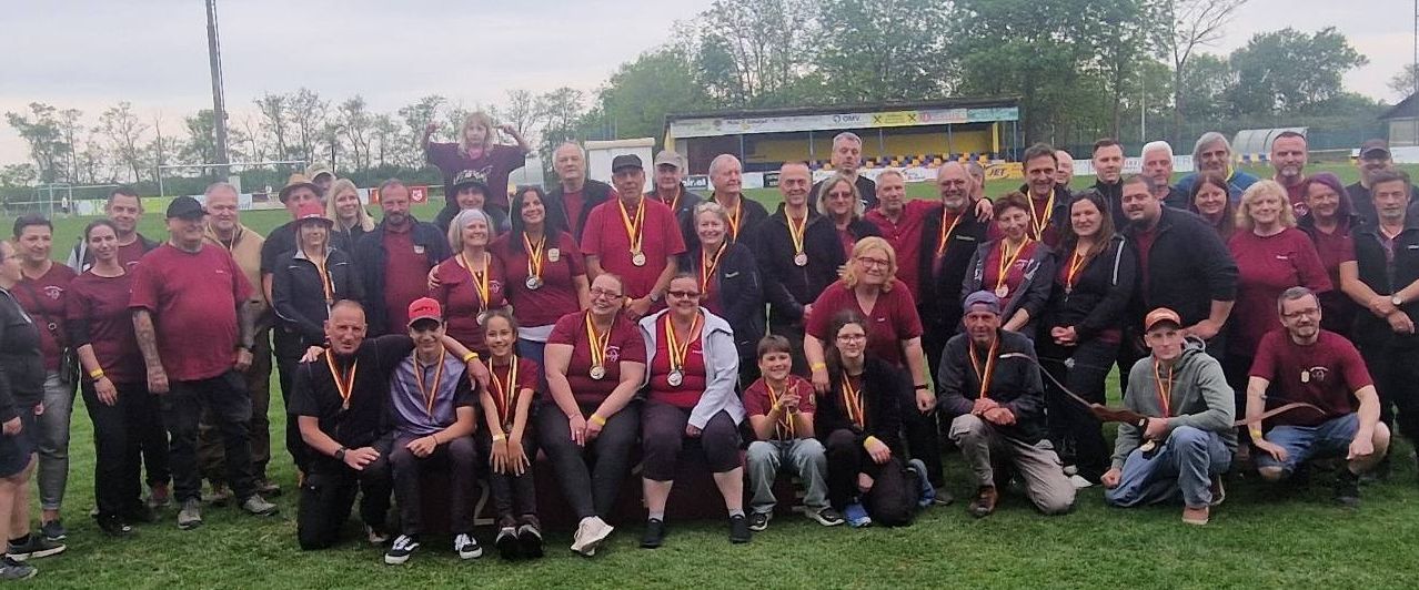 Group of people in maroon shirts pose with medals on a field. A child stands on a man's shoulder.