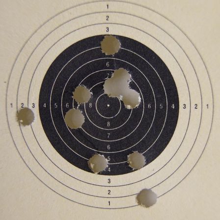 Ein Nahaufnahme eines Ziels mit mehreren Einschusslöchern, nummeriert von 1 bis 10. Der zentrale Anschlag ist größtenteils intakt, mit Löchern in den äußeren Ringen.