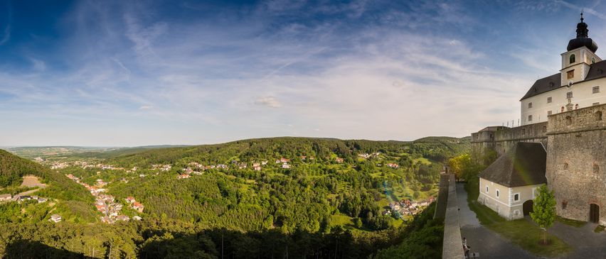 Luftaufnahme eines Dorfes mit vielen Häusern, eingebettet in einem üppig grünen Tal unter einem klaren blauen Himmel.