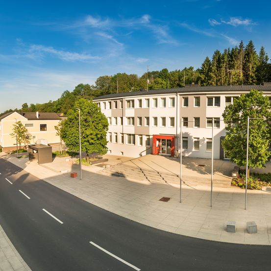 Eine Luftaufnahme eines Gebäudes mit einer roten Tür und weißen Wänden, umgeben von Bäumen, an einem sonnigen Tag.