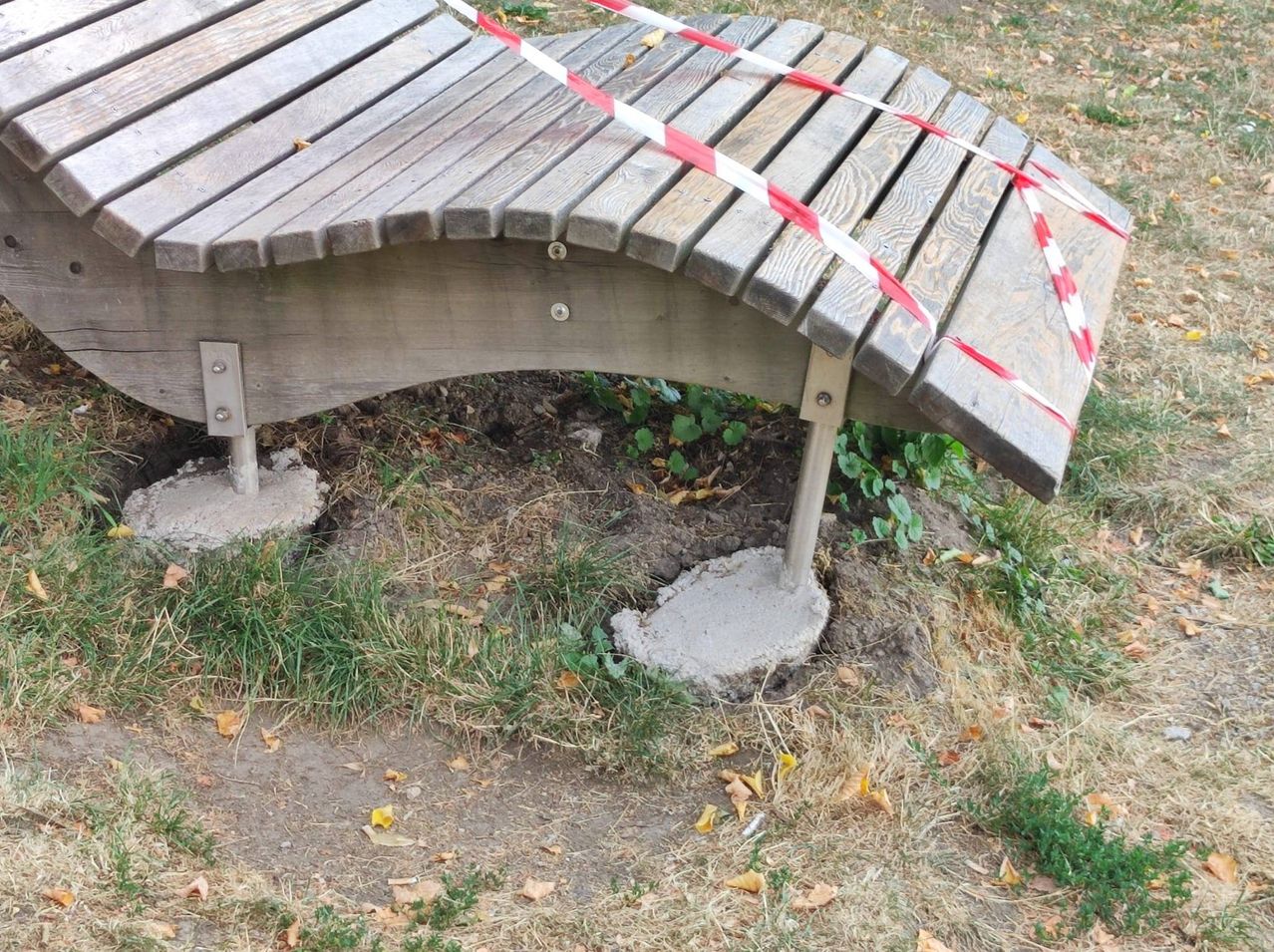 Eine Holzbrücke mit rot-weißem Absperrband, teilweise im Boden vergraben.