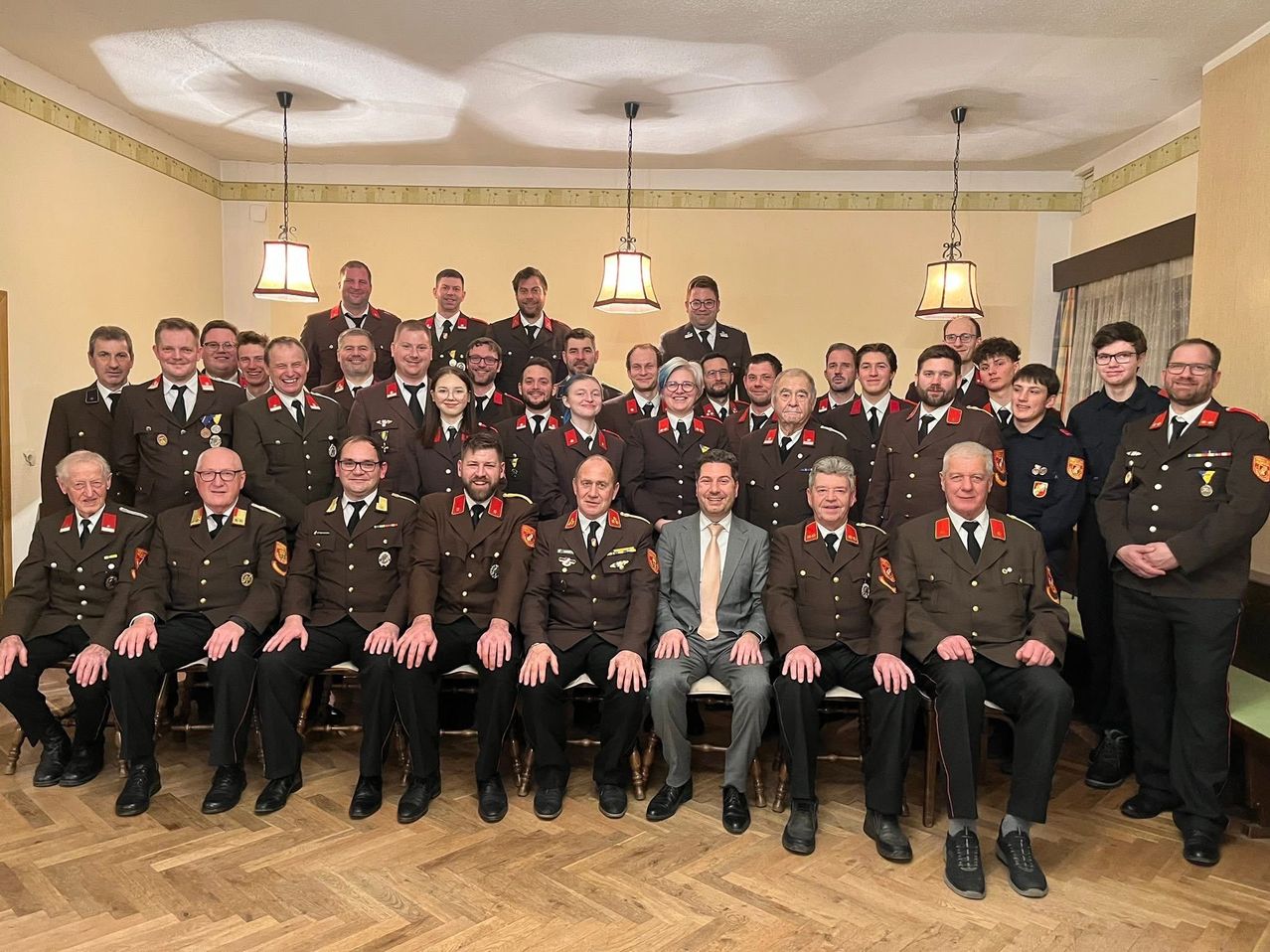 Eine Gruppenaufnahme von Personen in Uniform, die in Reihen stehen und sitzen, mit einer Person in Anzug in der Mitte.