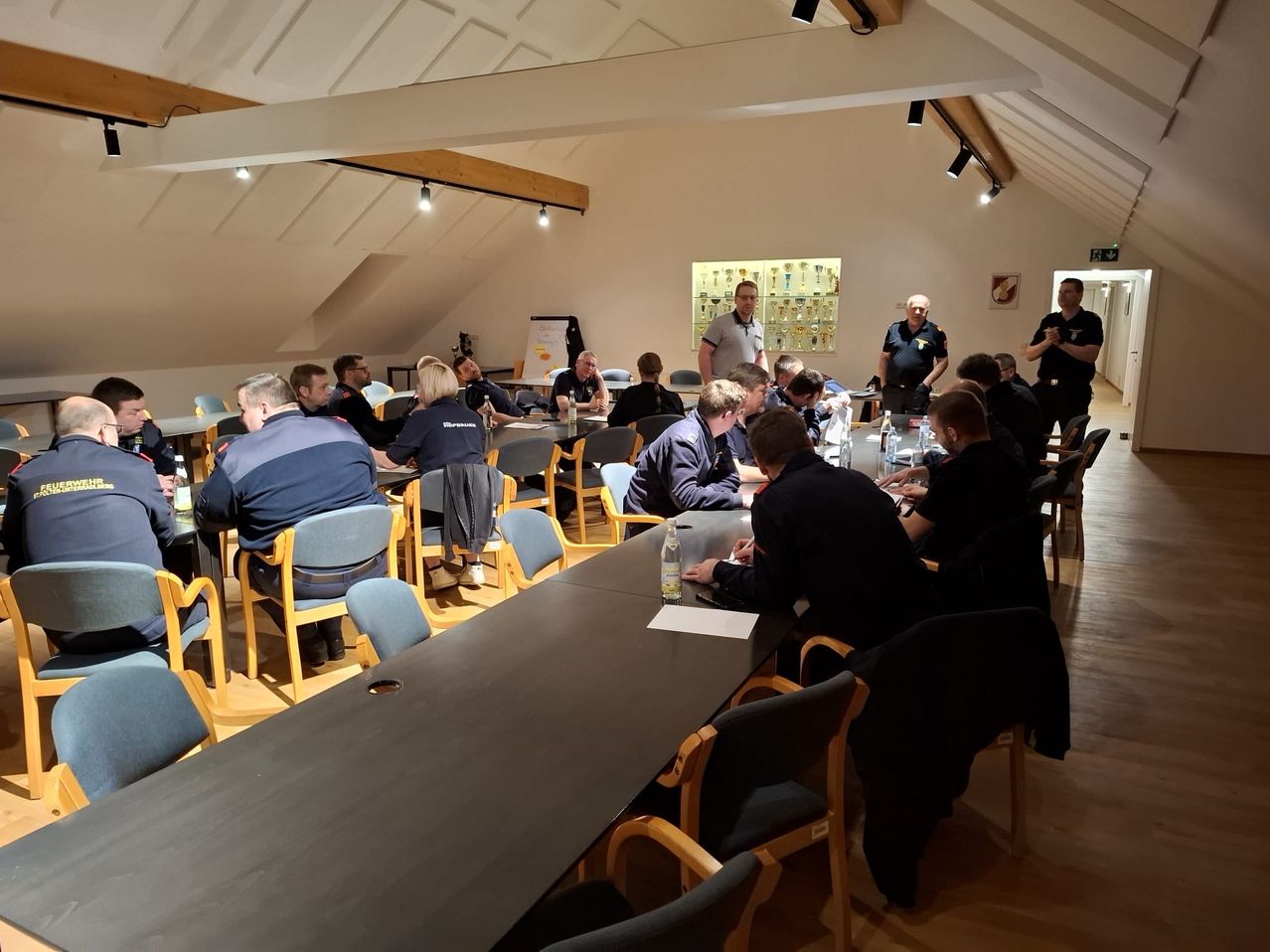 Eine Gruppe von Menschen sitzt um einen Tisch in einem Raum mit Holzboden und einer Glasvitrine. Sie führen eine Diskussion.