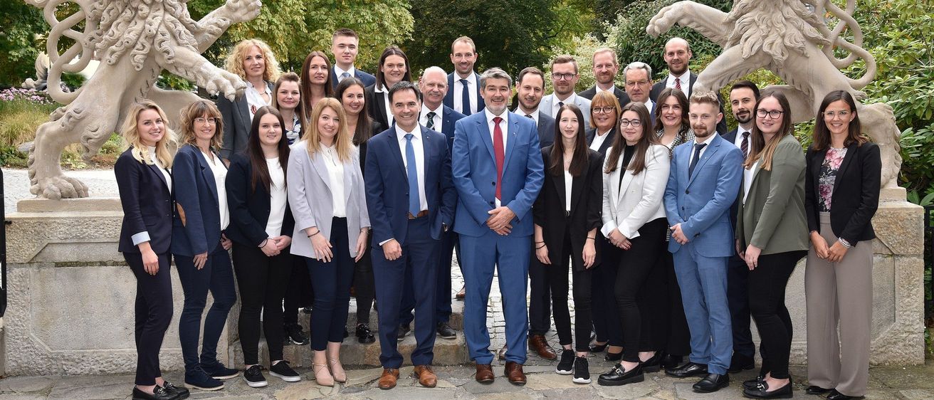 Eine Gruppe von Geschäftsleuten in formeller Kleidung posiert für ein Foto vor zwei Löwenstatuen.