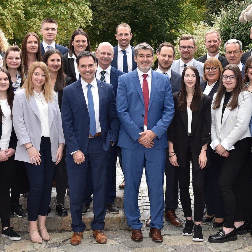 Eine Gruppe von Geschäftsleuten in formeller Kleidung posiert für ein Foto vor zwei Löwenstatuen.