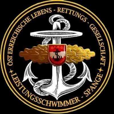 Ein kreisförmiges Emblem zeigt einen Anker mit einem Schild in der Mitte, umgeben von einem Lorbeerkranz. Der Schild trägt ein Logo mit der Aufschrift 'O.R.G.' über einem Kreuz. Die Worte 'Osteriche Lebens' und 'Rettungs' sind oben eingraviert, und 'Helfer Schwimmer' und 'Spange' sind unten.