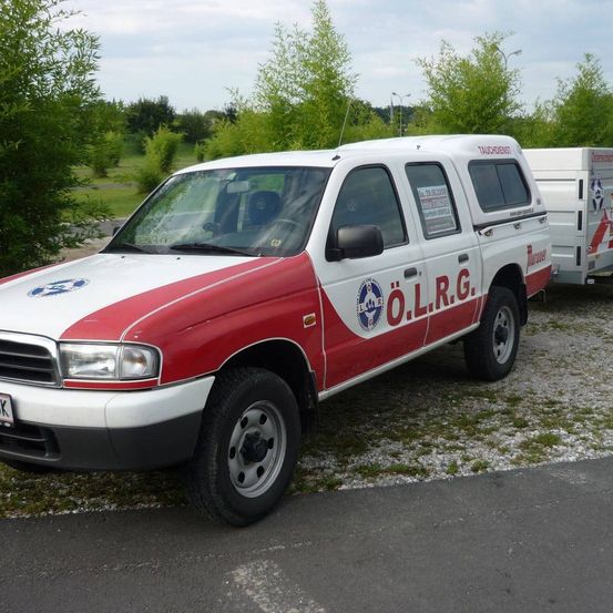 Ein rot-weißer LKW mit der Aufschrift O.L.R.G. am Straßenrand geparkt, mit einem Anhänger dahinter.