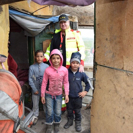 Ein Mann in einer Warnweste steht mit drei Kindern vor einer Unterkunft, ein Kinderwagen neben ihnen.