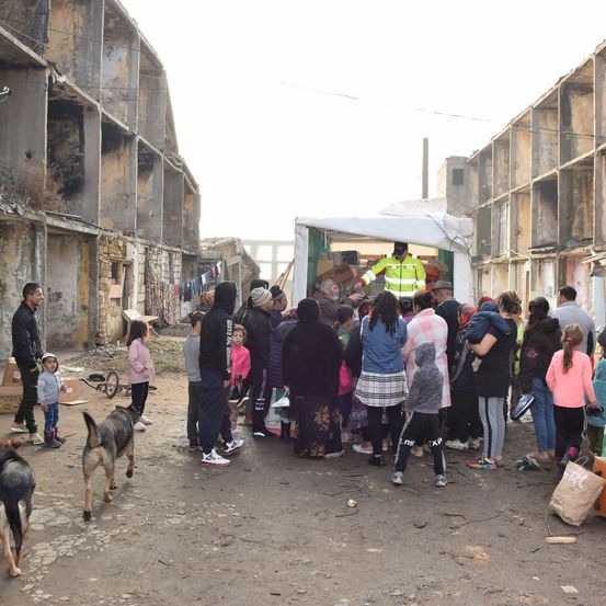 Eine Gruppe von Menschen steht in einer Schlange vor einem alten Gebäude. Ein Mann in einer Warnweste verteilt Gegenstände an die Menge.