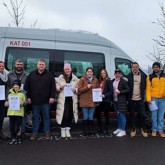 Eine Gruppe von Menschen, Erwachsene und Kinder, posiert für ein Foto vor einem Bus, hält Urkunden und trägt Winterkleidung.