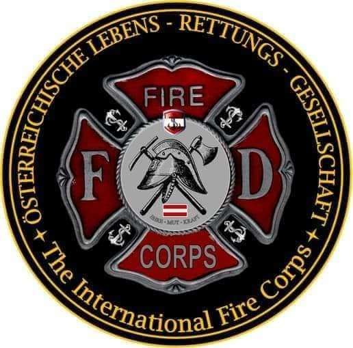 Das Emblem des Internationalen Feuerwehrkorps zeigt einen Schild mit den Buchstaben F und D, Hammer und Axt und einem Helm. Die Worte 'Feuer' und 'Corps' sind prominent dargestellt. Das Emblem ist von einem goldenen Rand umrahmt.