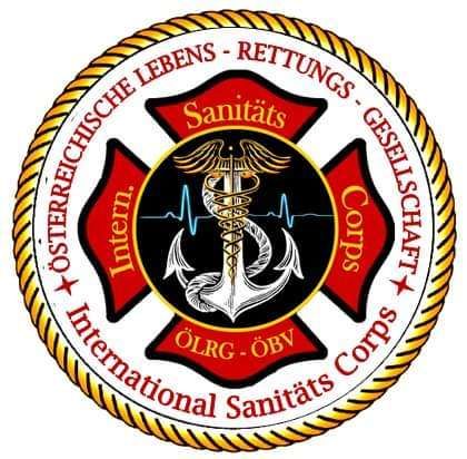 Das Emblem zeigt einen roten Hintergrund mit schwarzem Rand und einem gelben Seildesign. Es enthält ein Kreuz, ein medizinisches Symbol und die Texte 'Sanitas' und 'International Sanitas Corps'. Die Wörter 'Int.' und 'ÖLRG - ÖBV' sind ebenfalls vorhanden.