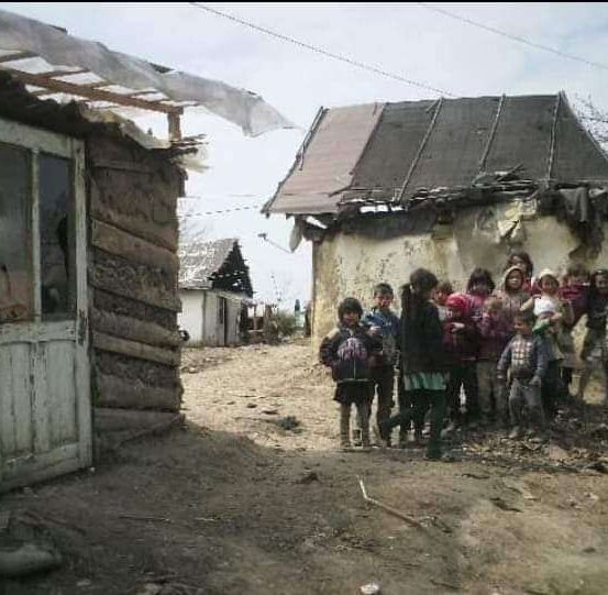 Eine Gruppe von Kindern steht vor einem verwitterten Gebäude mit einem beschädigten Dach in einem ländlichen Gebiet.