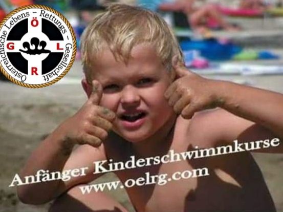 Ein kleiner Junge am Strand, lächelt und hat beide Hände an den Ohren, trägt eine Schwimmkappe, mit einem Logo in der oberen linken Ecke.