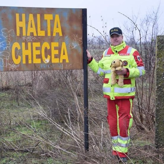 Ein Mann in einer reflektierenden Warnweste steht neben einem Schild mit gelber Graffiti. Das Schild zeigt 'HALTA CHECEA'.