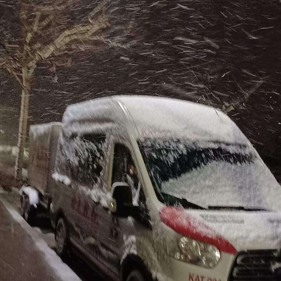 Ein weißer Van, der mit Schnee bedeckt ist, steht auf einem Bordstein. Er hat einen roten Streifen entlang der Seite.