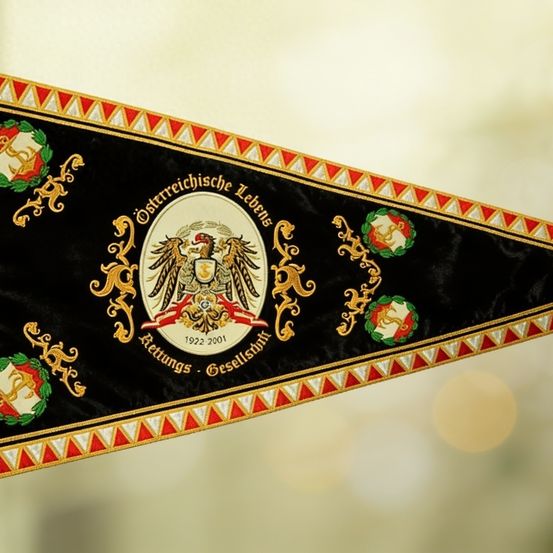Ein schwarzer und goldener Samtbanner mit Logo und Text. Das Logo zeigt einen Doppeladler, und der Text lautet 'Osterreichische Lebens' und '1922-2001'. Der Banner hat goldene Dekorationen und Ränder.